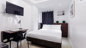 Quarto moderno com cama, escrivaninha com laptop, televisão na parede e janela com cortinas.