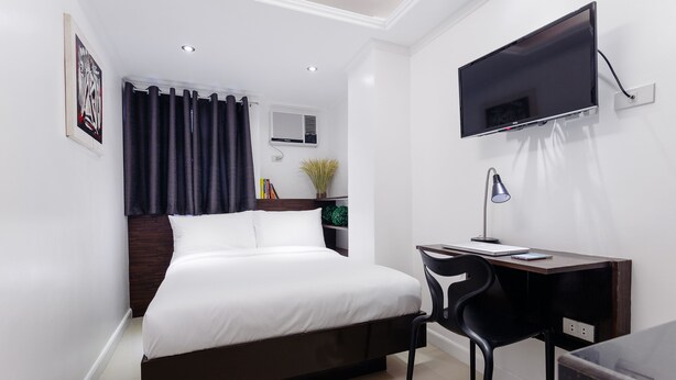 Quarto de hotel moderno com cama, escrivaninha, cadeira, televisão e planta em vaso.