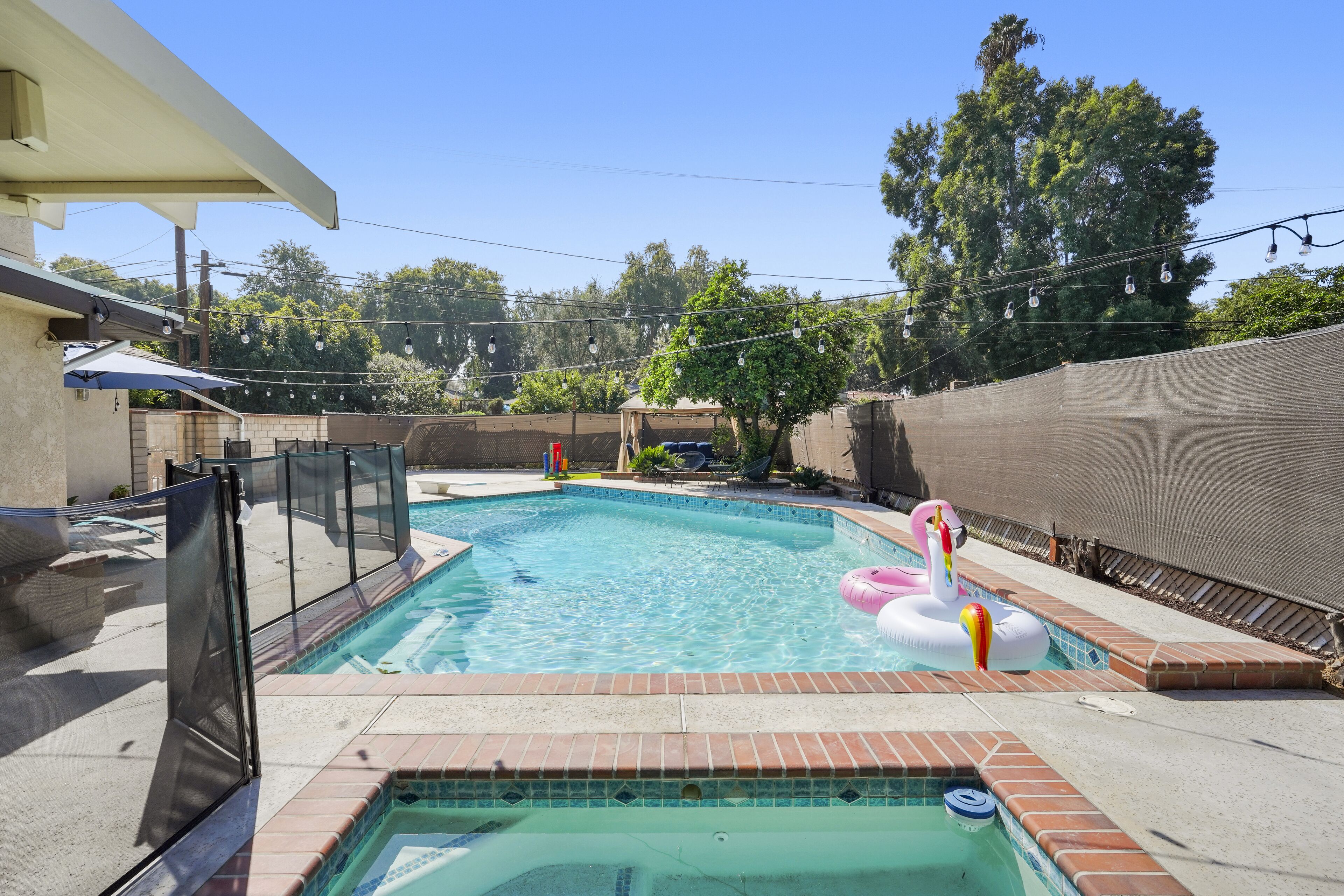 Piscina con jacuzzi, rodeada por un muro de ladrillo y un área de patio techada.