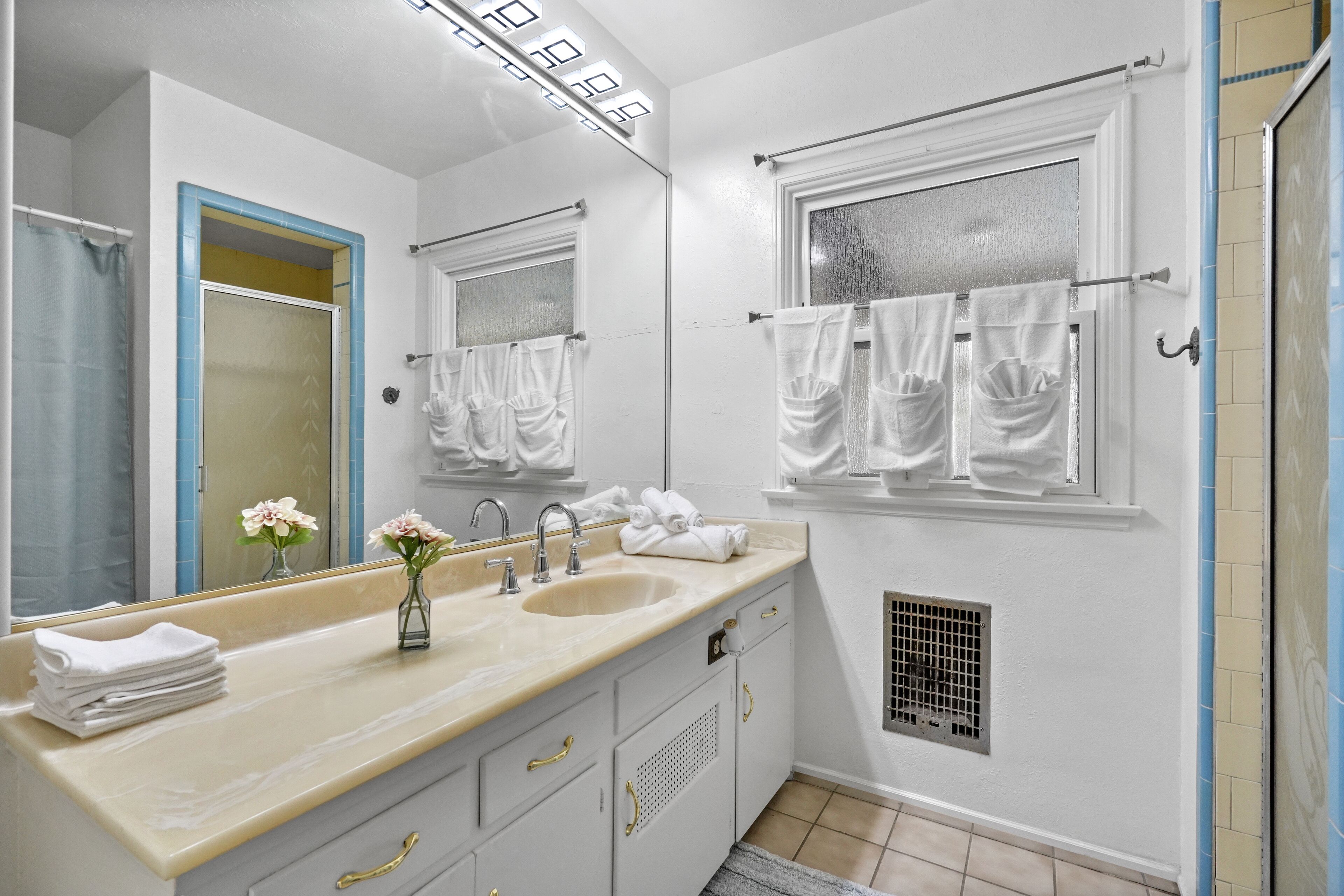 Une salle de bain avec un double lavabo, un miroir, une fenêtre avec un porte-serviettes et un espace douche.