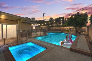 Un jardin avec une piscine, un jacuzzi et un espace salon couvert.