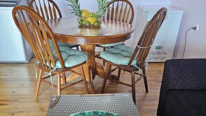A dining area with a round table, four wooden chairs, and a bowl of fruits and flowers on a mat.