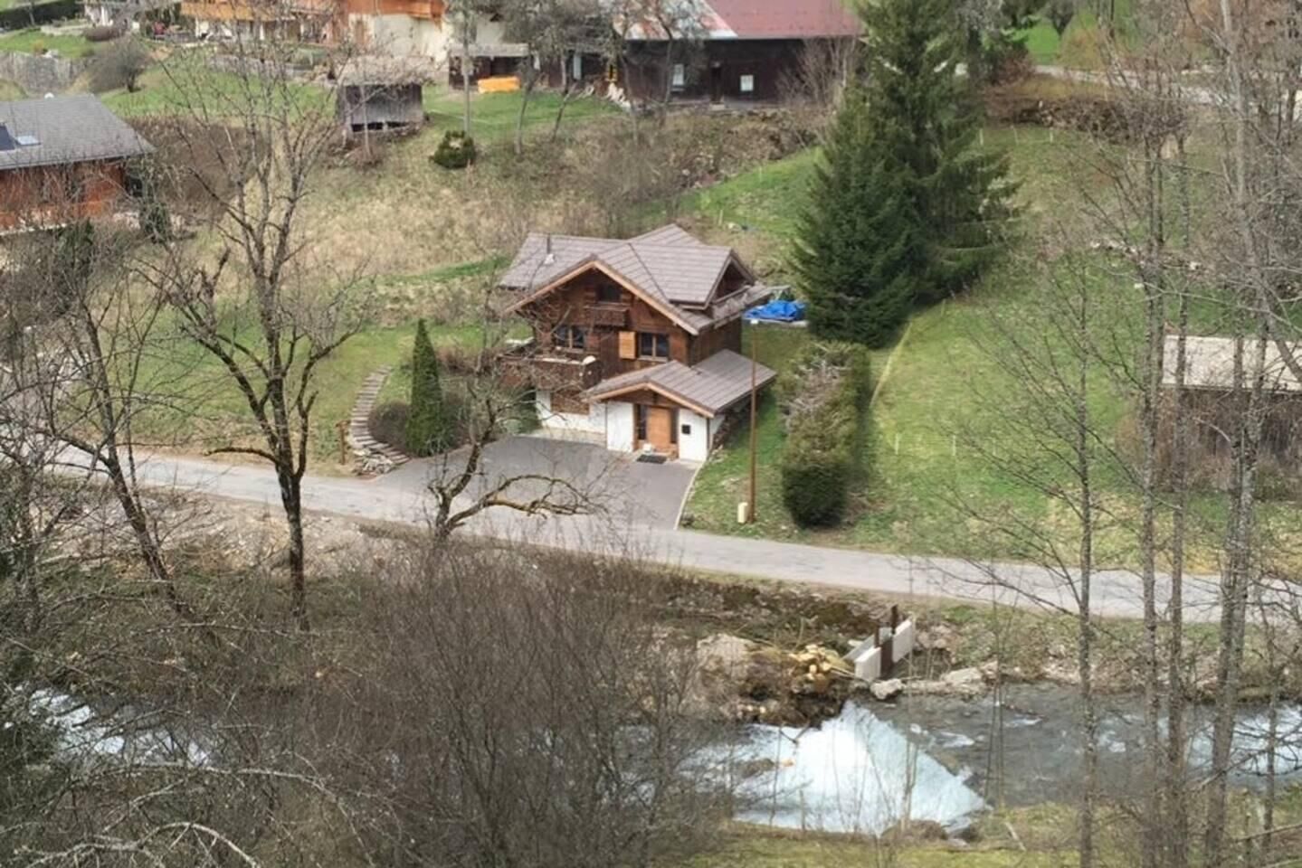 A house with a sloped roof, a front porch, and a driveway leading to a river.