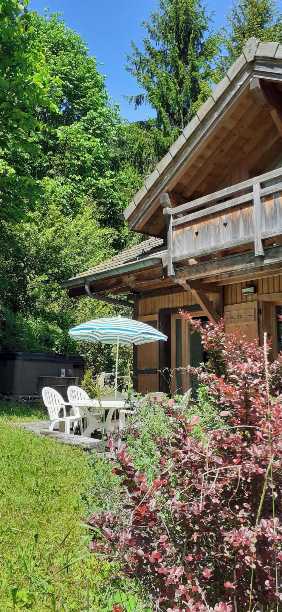 Une cabane en bois dotée d’un balcon, entourée d’une végétation luxuriante et agrémentée d’une terrasse avec des meubles d’extérieur.