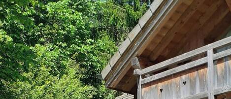Une cabane en bois dotée d’un balcon, entourée d’une végétation luxuriante et agrémentée d’une terrasse avec des meubles d’extérieur.