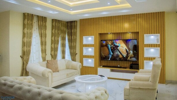 Ein modernes Wohnzimmer mit einer Couch, Sesseln, einem Couchtisch und einem flachbildfernseher, der an einer Holzwand angebracht ist.