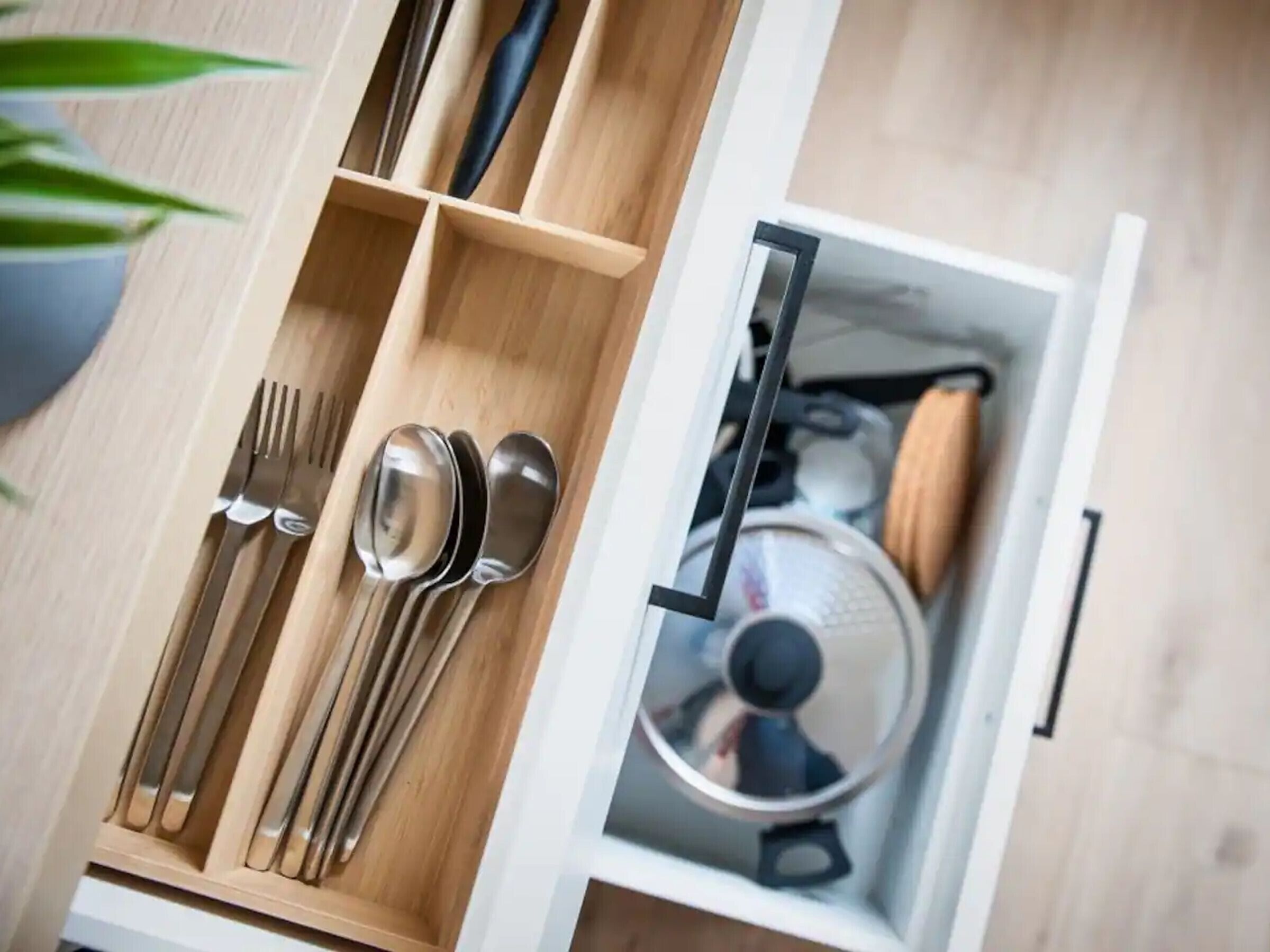 A drawer with utensils and a pot.