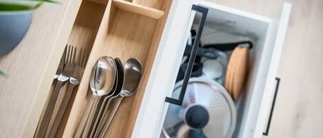 A drawer with utensils and a pot.