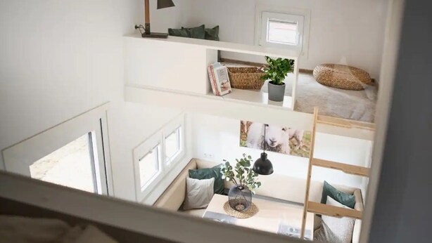Een kamer met meerdere verdiepingen, voorzien van een stapelbed, een bureau, een lamp, een plant en een raam.
