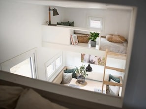 Quarto com vários níveis, incluindo uma cama beliche, escrivaninha, luminária, planta e janela.