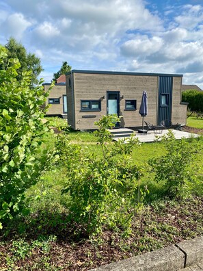 A modern two-story house with a flat roof, a front door, and a small porch with outdoor seating. - Holiday Home 'Tiny House Raum Käpsele' with Private Terrace, Wi-Fi and Air Conditioning (Laichingen)