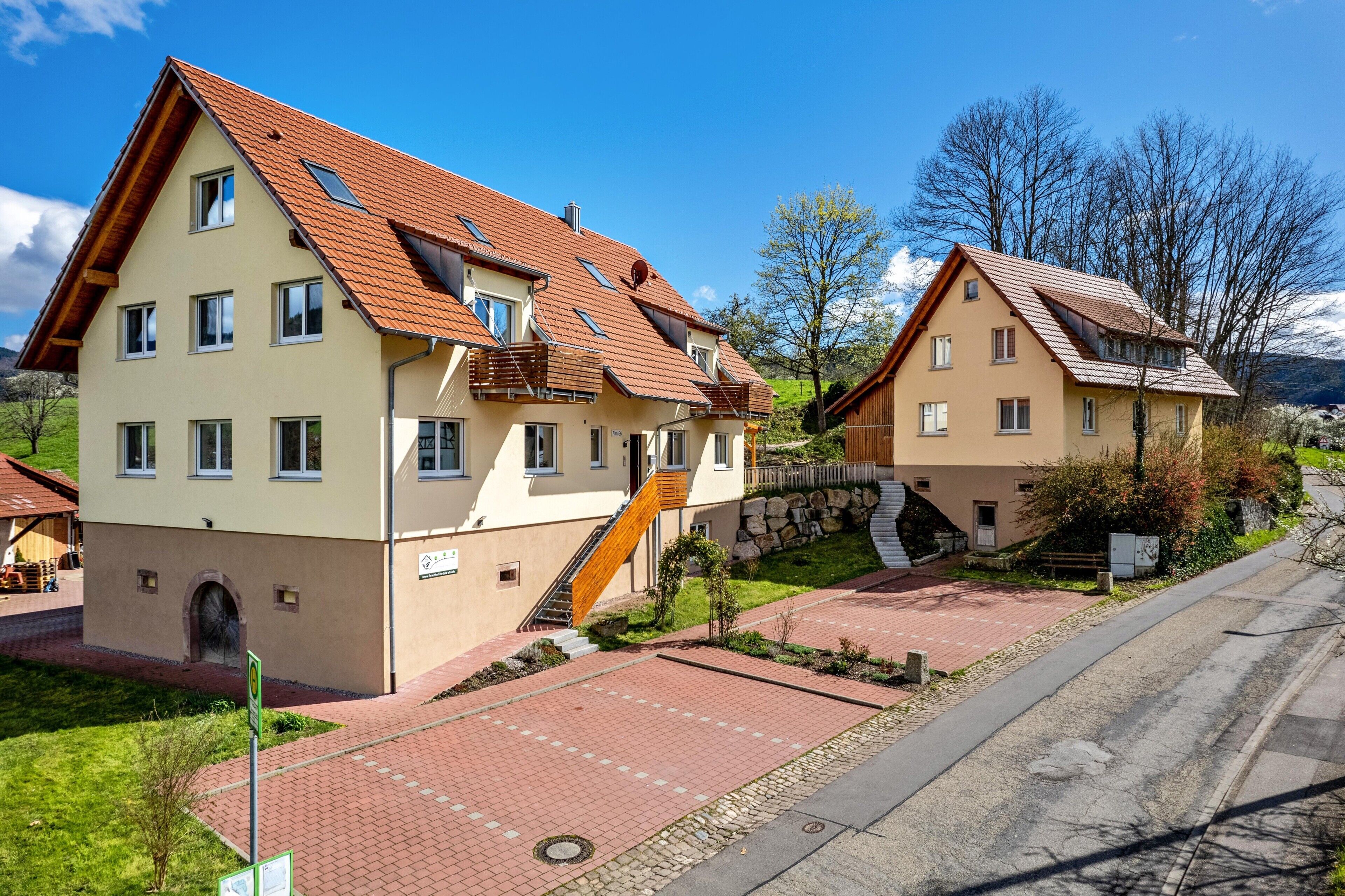 A two-story residential building with a sloped roof, a staircase leading to the upper floor, and a paved driveway.
