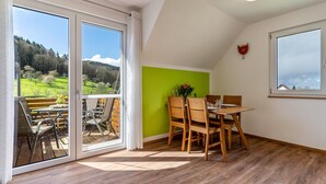 A room with a dining table, chairs, a green accent wall, and large sliding glass doors leading to an outdoor area with a view of a green landscape. - Apartment "Lieselotte, 72 sqm" with Balcony and Wi-Fi (Oberkirch)