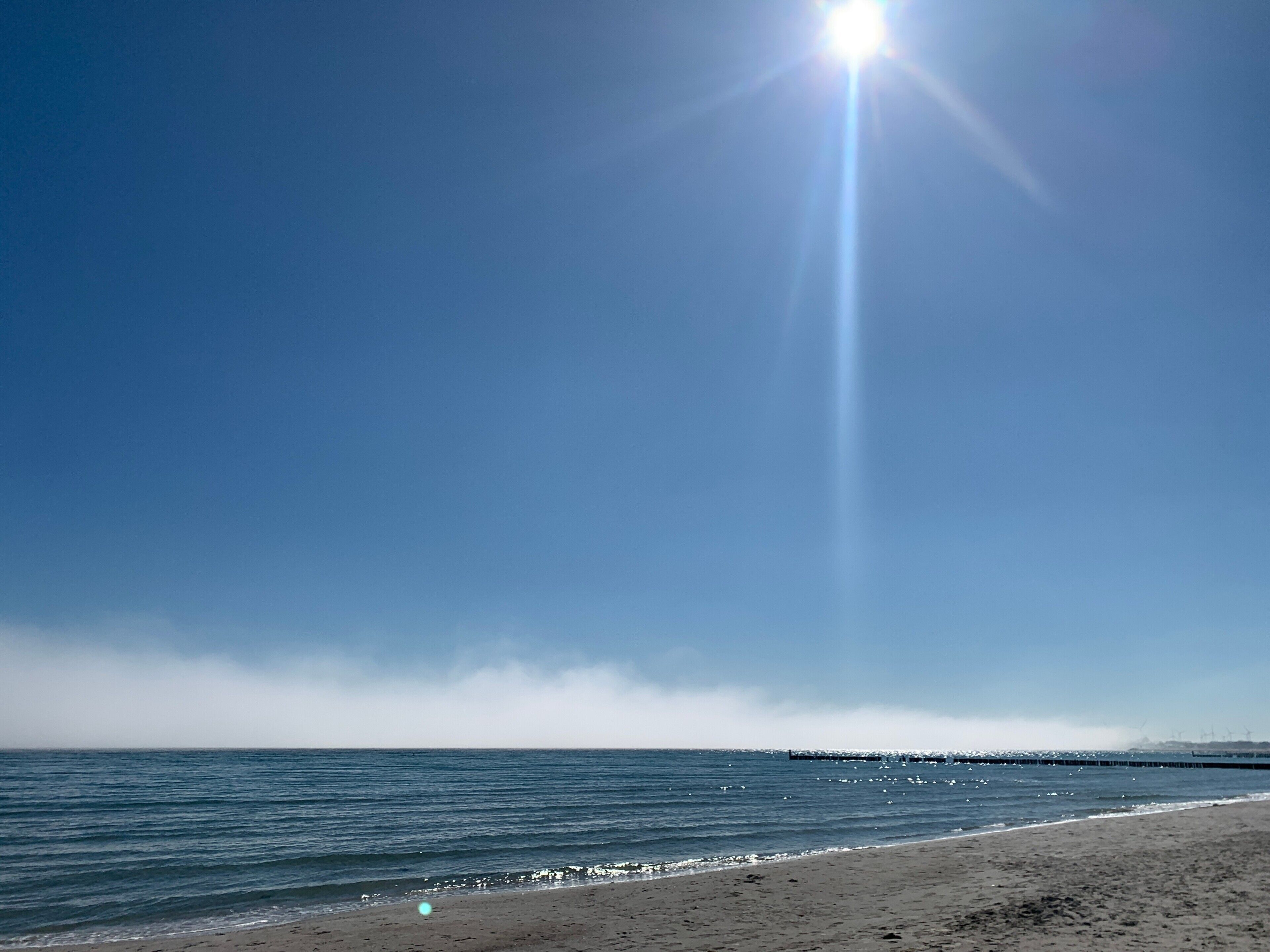 Ein Strand mit blauem Himmel, ruhigem Meer und einem entfernten Steg.