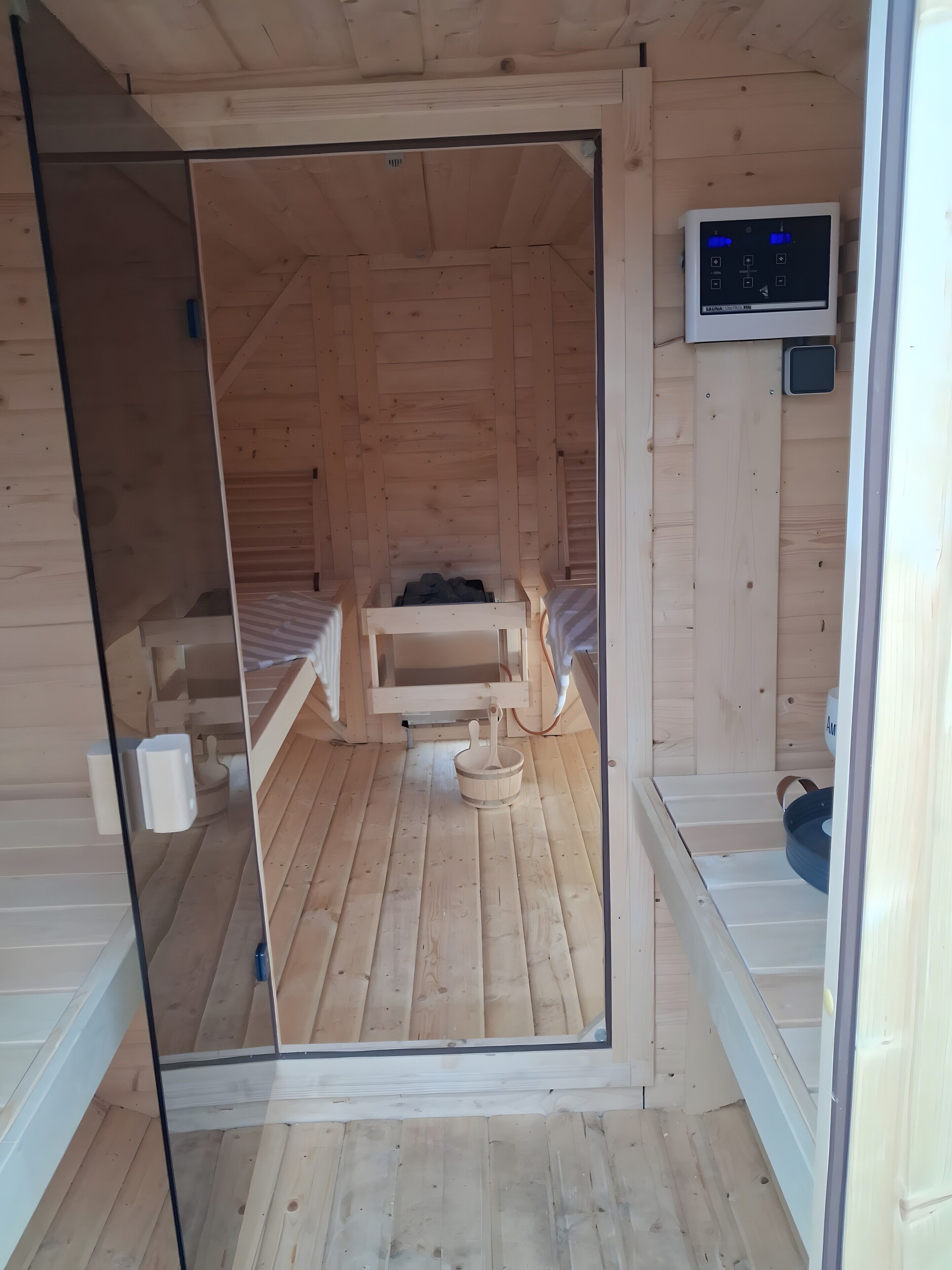 En stuga av trä med en glasdörr, en säng, ett litet bord och en kontrollpanel på väggen.