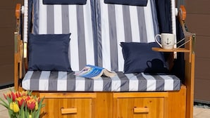 Ein gestreiftes Outdoor-Sofa mit Kissen, ein kleiner Tisch mit einer Tasse und eine Vase mit Tulpen.