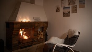 Ein Kamin mit einem Schild, ein Sessel mit einem Fellüberwurf und mehrere gerahmte Bilder an der Wand.