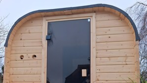 Eine Holzhütte mit einer großen Glasdoor, einem kleinen Fenster und einer Laterne auf dem Boden.