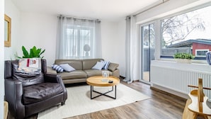 A living room with a leather armchair, a round wooden coffee table, a sofa, and a large window with a view of buildings. - Holiday Apartment "Salem´s Treasure Manor" with Private Terrace, Shared Garden & Wi-Fi (Salem)