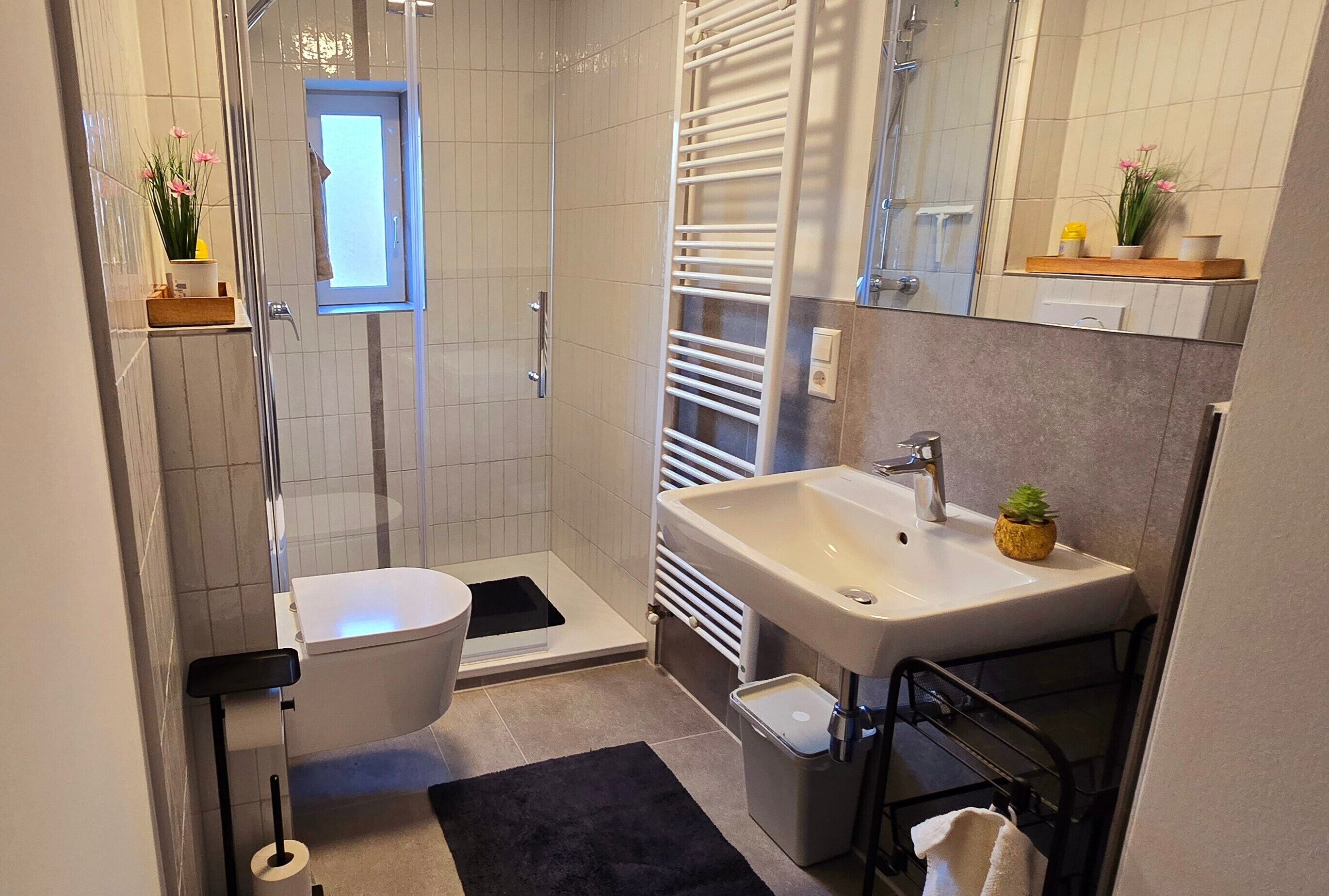Ein modernes Badezimmer mit Dusche, Toilette, Waschbecken und einem kleinen Fenster.