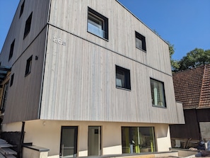 A modern building with a vertical wooden facade, multiple windows, and a flat roof.