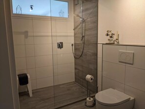 Un baño moderno con cabina de ducha de vidrio, un inodoro y un pequeño taburete.