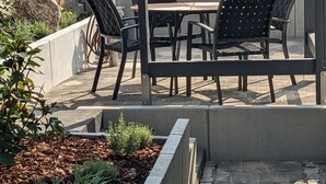 Une terrasse extérieure avec une table et des chaises, entourée d’un petit muret en pierre et de plantes.
