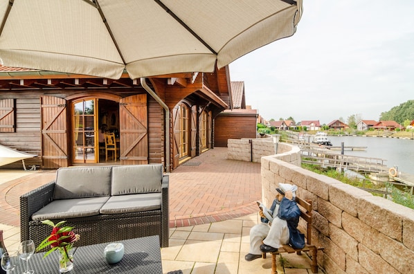 Ein Holzgebäude mit einer Terrassenfläche, einer Couch, einem Tisch mit einer Vase und einer Person, die auf einer Bank sitzt.