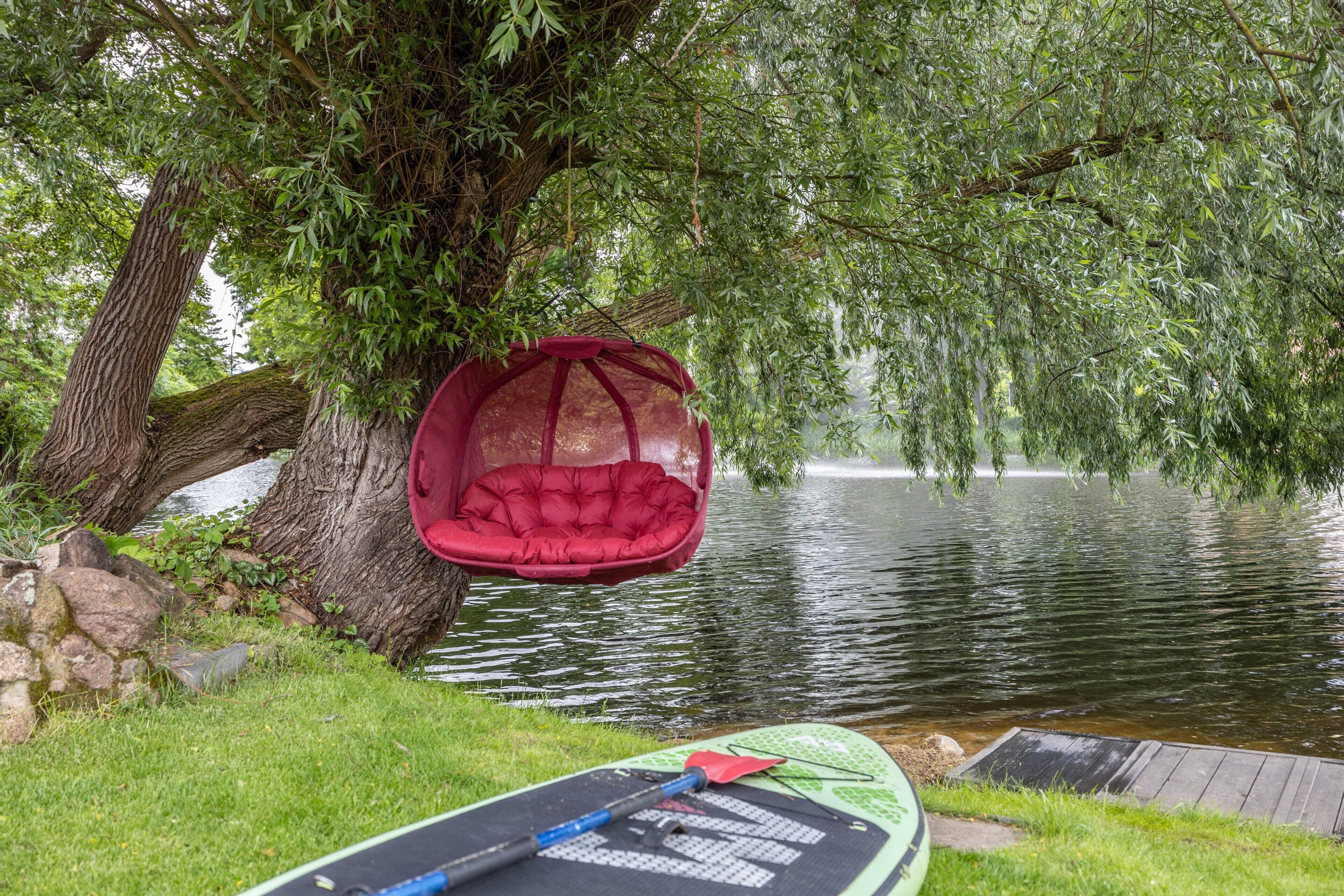 Un entorno tranquilo junto al lago con una hamaca roja y una tabla de remo.