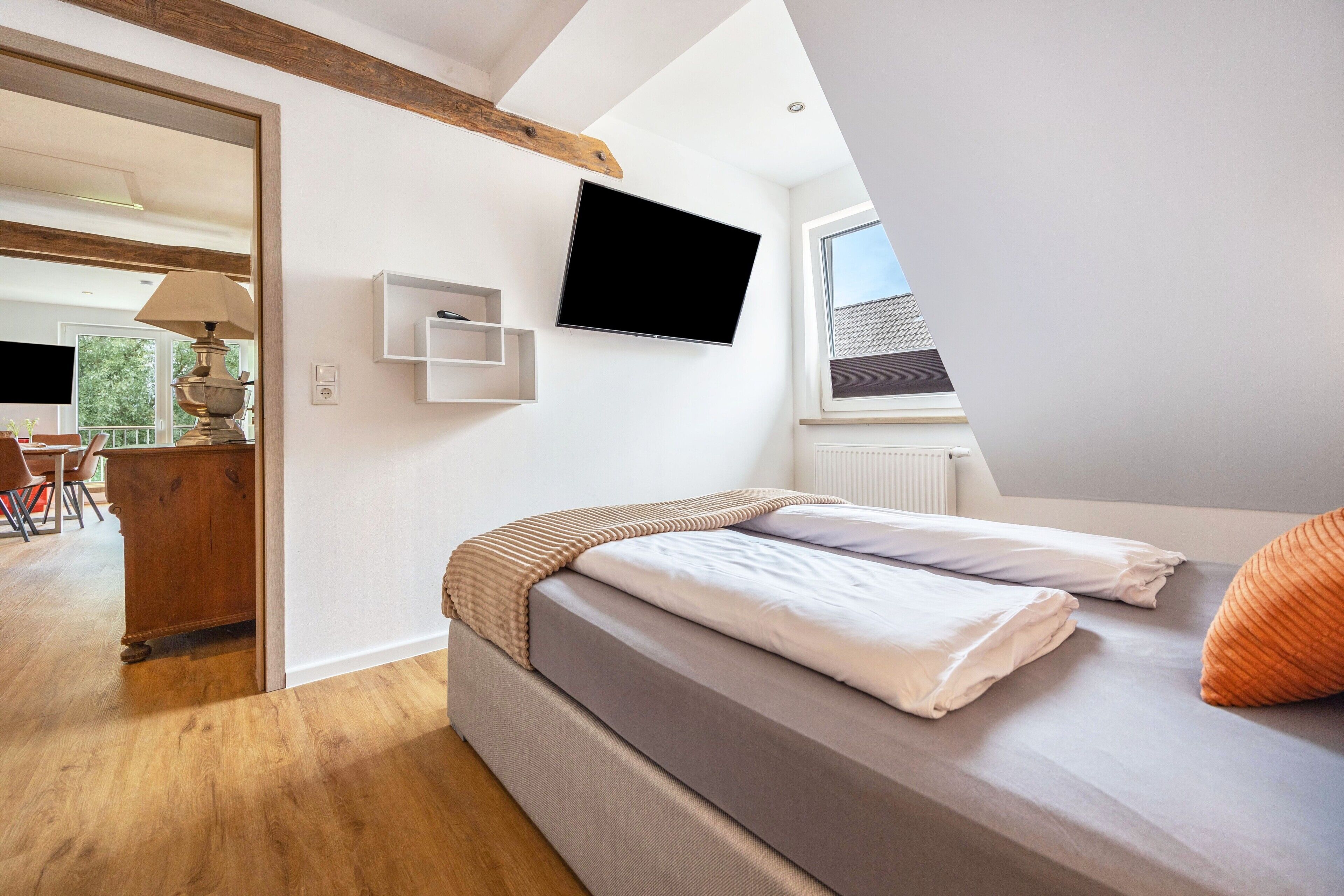 A bedroom with a bed, a TV, a window, and a view of the outdoors.