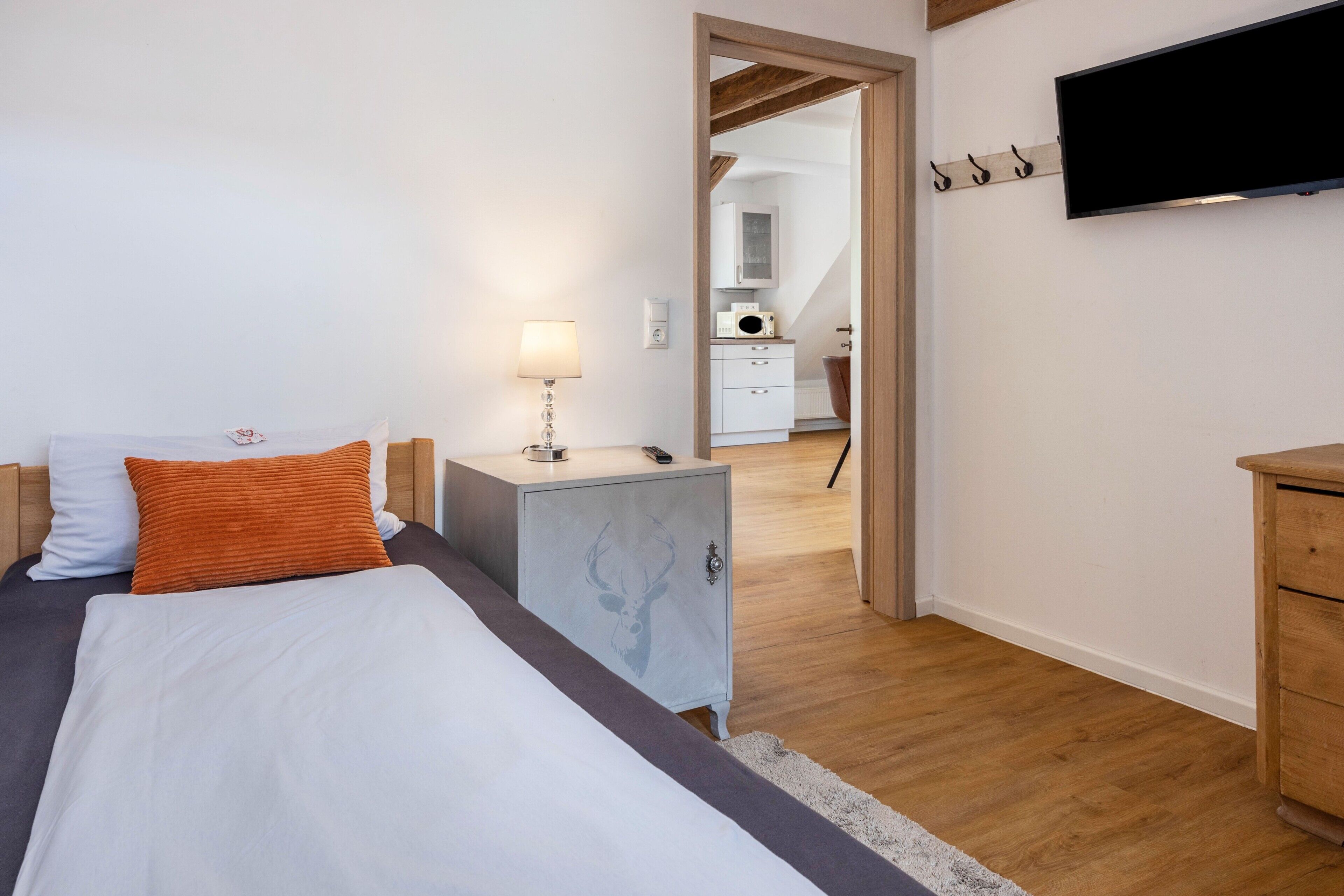 A bedroom with a bed, a nightstand, a TV, and a wooden floor.