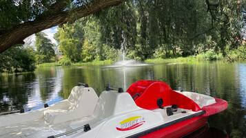 Um barco com esquema de cores vermelho e branco está atracado perto de um rio calmo, cercado por vegetação exuberante e árvores.