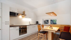 A modern kitchen with white cabinets, a built-in oven, and a dining area with a wooden table and chairs. - Apartment 2, 65sqm, 2 bedrooms, max. 4 persons (Schmallenberg)