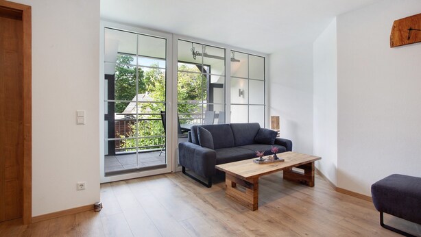 A modern living room with a sofa, a wooden coffee table, and a sliding glass door leading to a balcony. - Apartment 2, 65sqm, 2 bedrooms, max. 4 persons (Schmallenberg)