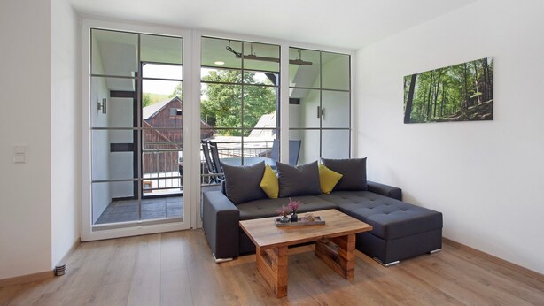 Ein modernes Wohnzimmer mit einer Eckcouch, einem Couchtisch aus Holz und einer großen Schiebetür zu einem Außenbereich.