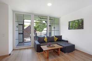 A modern living room with a sectional sofa, a wooden coffee table, and a large sliding glass door leading to an outdoor area. - Apartment 1, 76sqm, 2 bedrooms, max. 5 persons (Schmallenberg)
