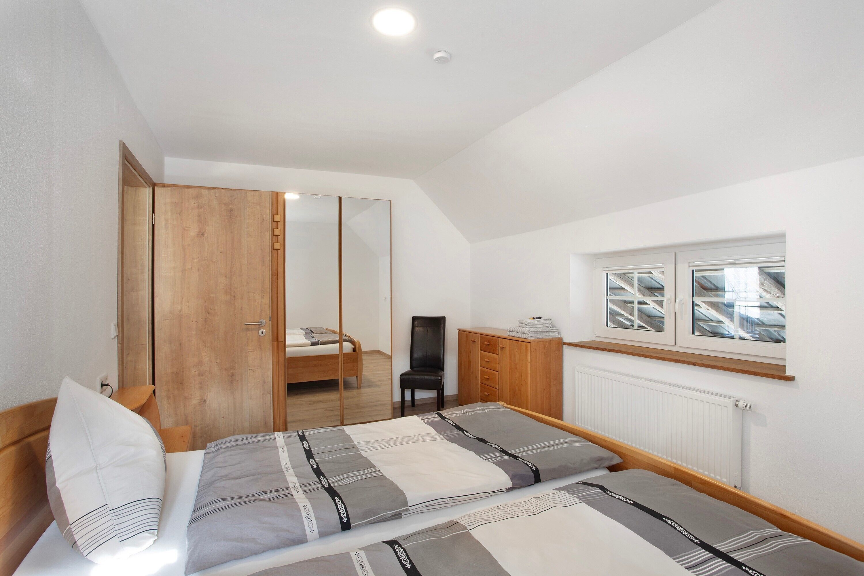 A bedroom with a bed, a chair, a wardrobe, a desk, and a window.