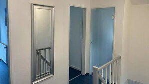 Un couloir aux murs blancs et aux portes bleues, qui mène à différentes pièces.
