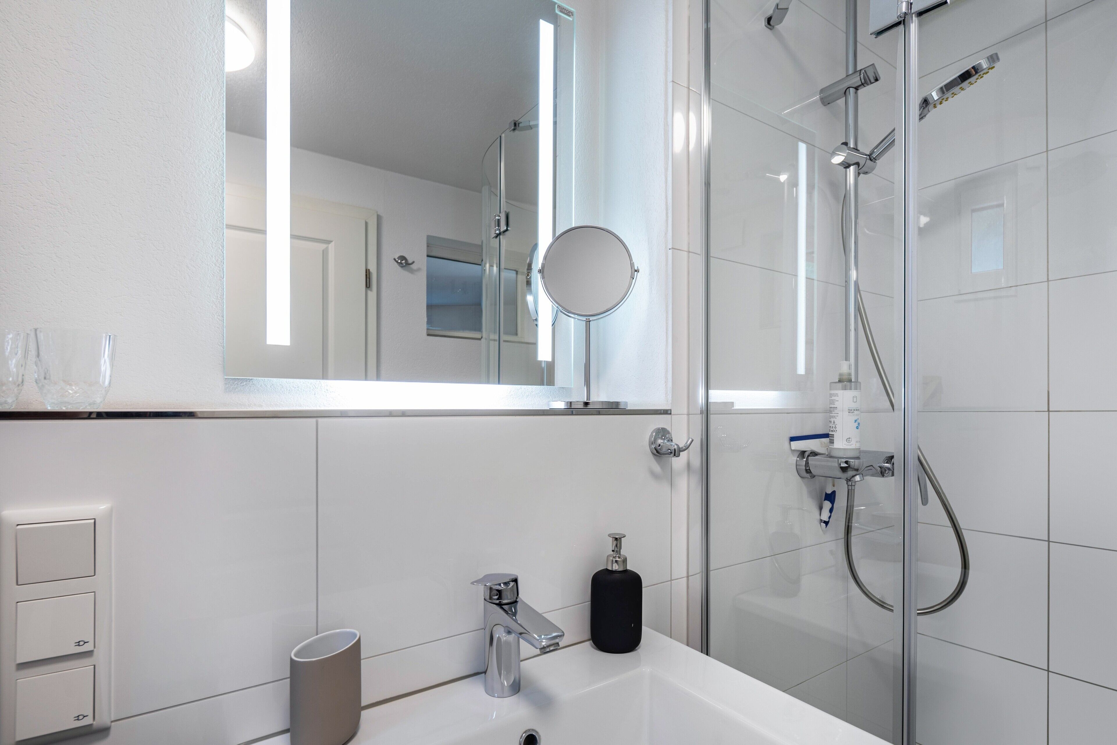 A modern bathroom with a glass shower enclosure, a white sink, a mirror, and a toilet.
