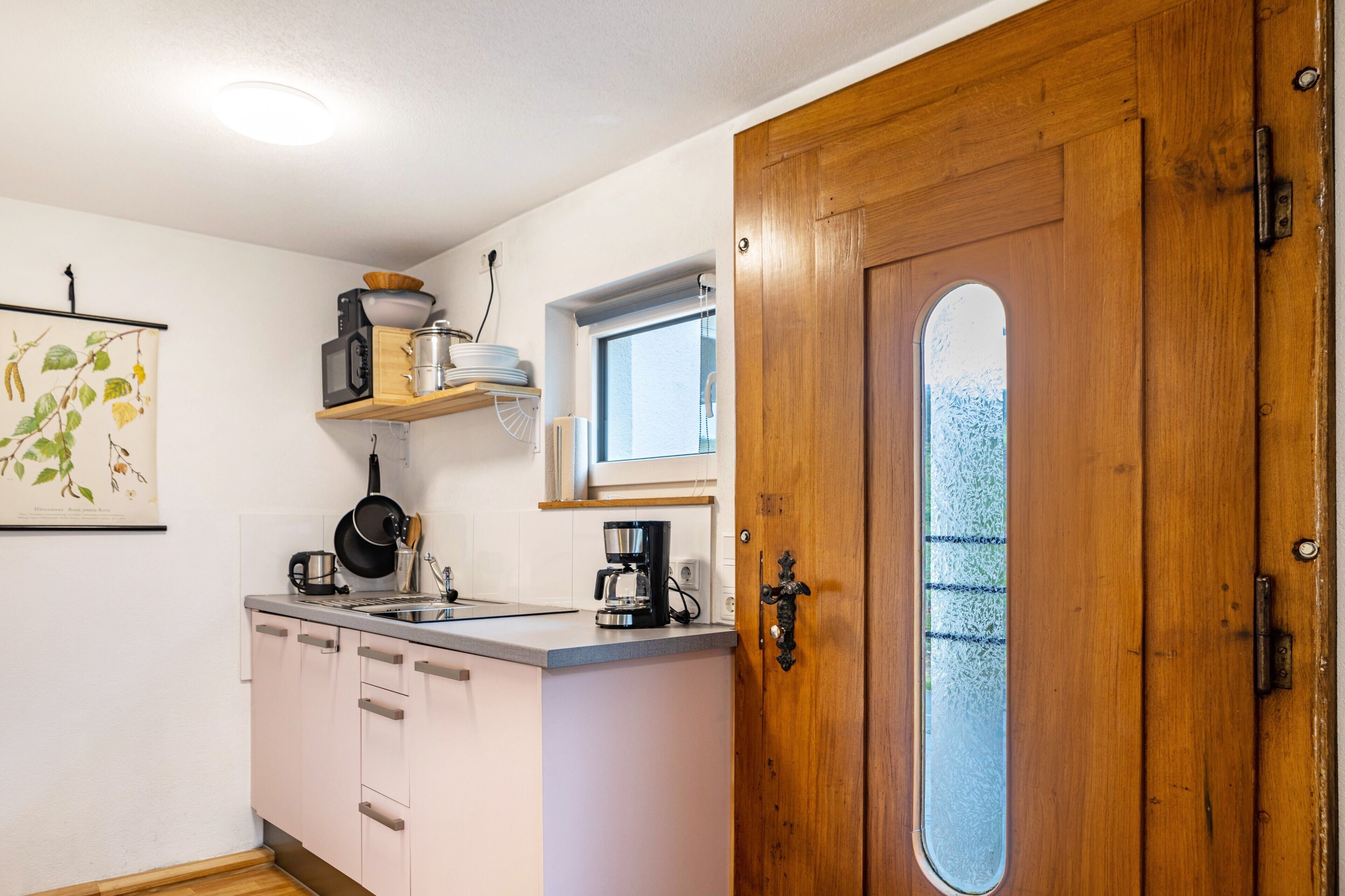 Een kleine keuken met een houten deur, een raam en een magnetron op een plank.