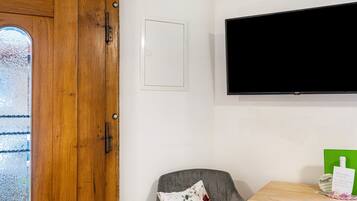 Ein Zimmer mit Holztür, einer weißen, wandmontierten Fernseher, einem grauen Sessel mit Blumenkissen und einem Holztisch mit einer grünen Ordner und einer Karte.
