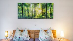 Une chambre avec une tête de lit en bois, deux lampes de chevet et un grand tableau représentant une forêt, placé au-dessus du lit.