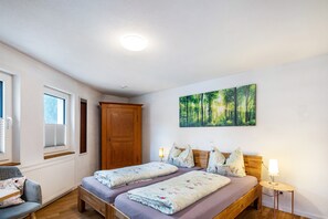 Un dormitorio con dos camas, un armario de madera, una ventana con persianas y un cuadro de un bosque.