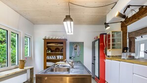 Une cuisine dotée d’un évier en acier inoxydable, d’étagères en bois, d’un réfrigérateur rouge et d’un luminaire suspendu.