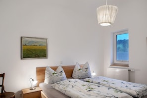 A bedroom with a bed, bedside table, lamp, and a window with a view of the outdoors. - Apartment 'Eiche Im Sand 68' with Shared Garden, Balcony and Wi-Fi (Steinau an der Straße)