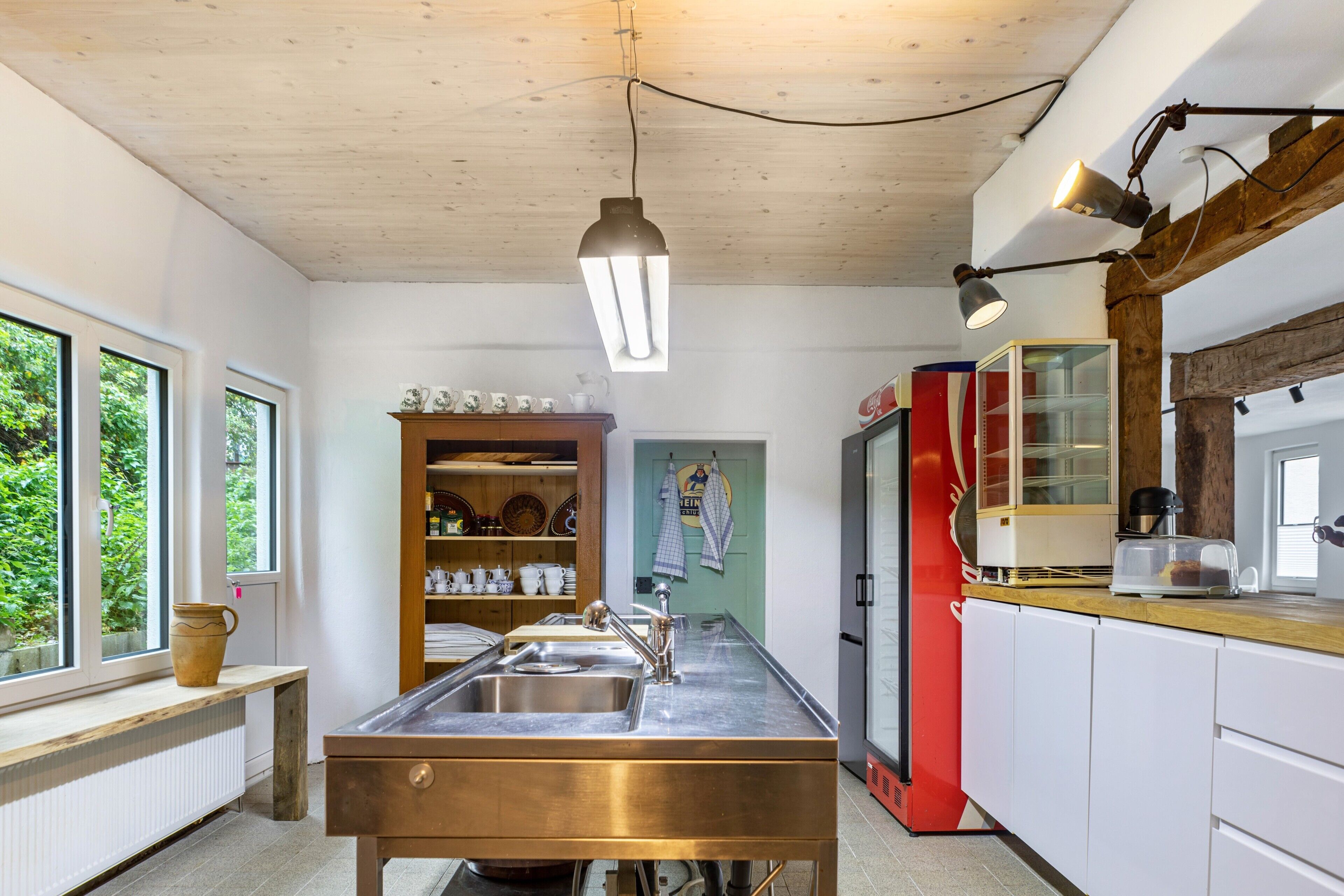 A kitchen with a stainless steel sink, wooden shelves, a red refrigerator, and a hanging light fixture.