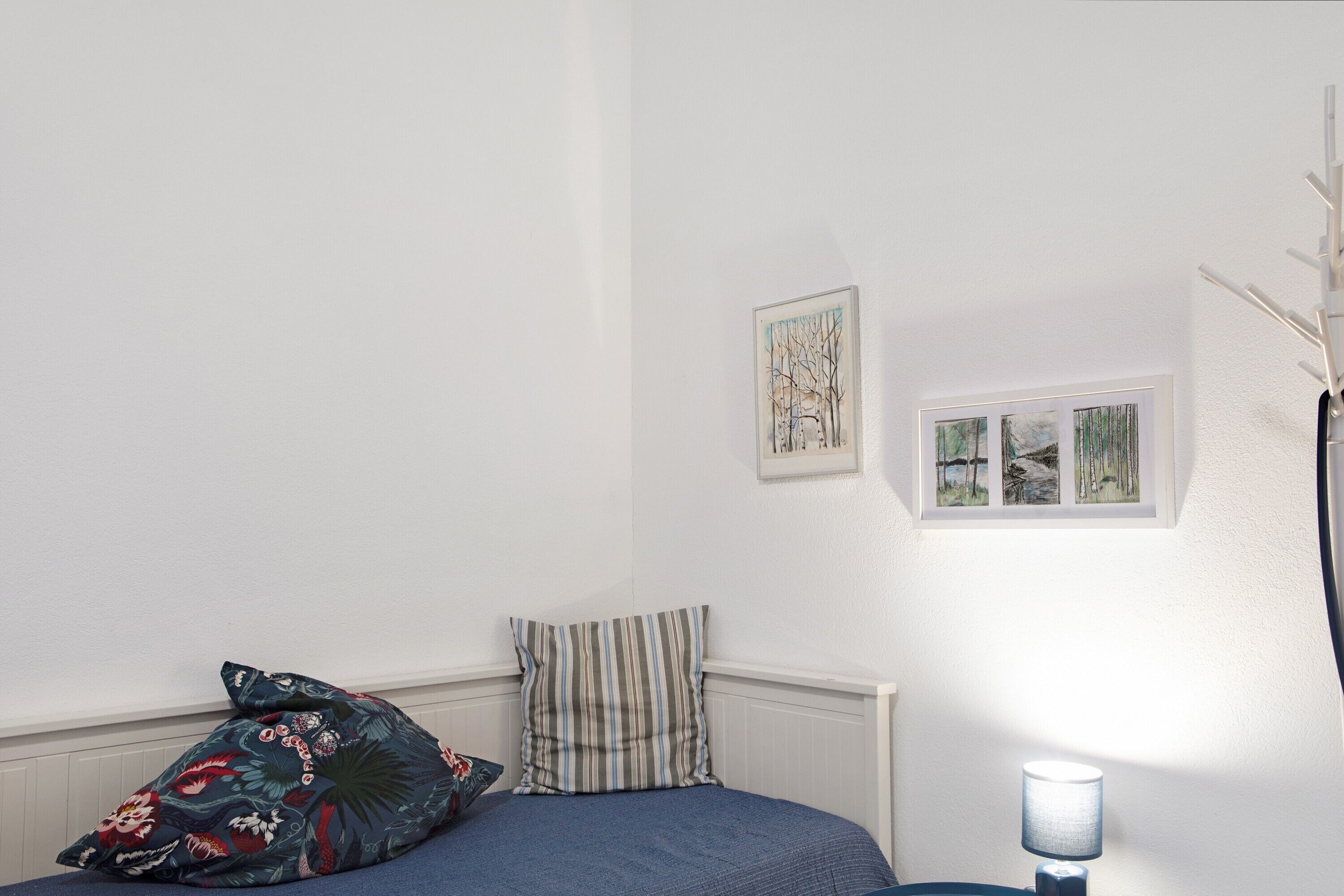 Une chambre à coucher avec un lit, des oreillers, une lampe de chevet et des œuvres d’art murales.