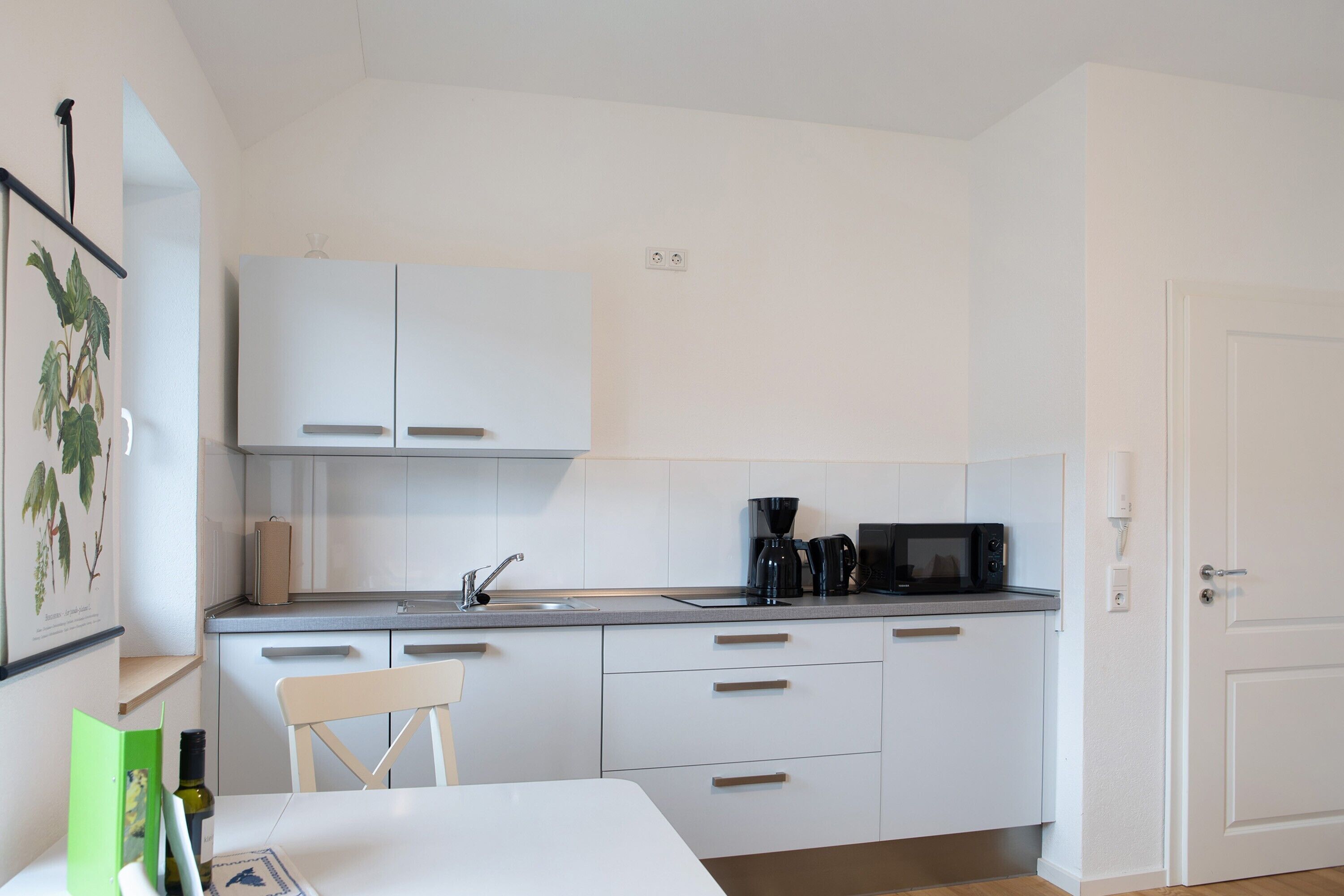 Una cocina moderna con armarios blancos, cafetera y microondas.