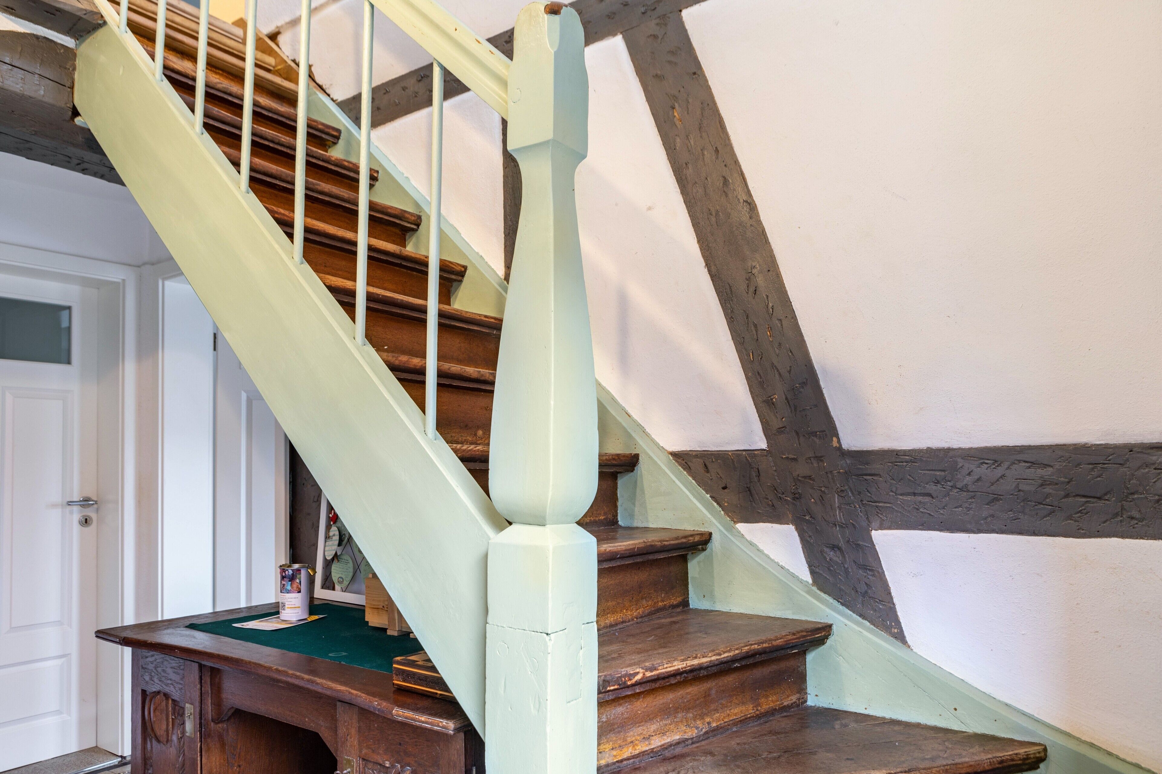 Eine Treppe mit Holzbodenstufen und einem hellgrünen Geländer, die zu einem Raum mit einer weißen Tür und einem grünen Teppich führt.