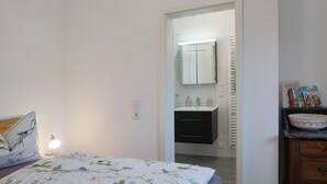 Une chambre à coucher comprenant un lit, une lampe de chevet, une table de chevet, une commode et une salle de bain avec un lavabo et un miroir.
